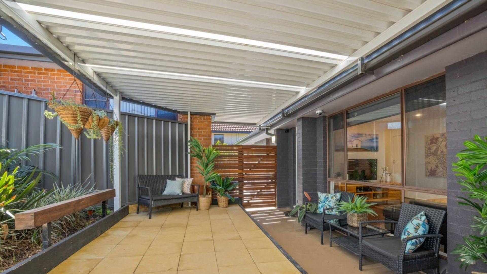 A covered patio area with outdoor seating, a brick wall, and a glass door leading to the interior.