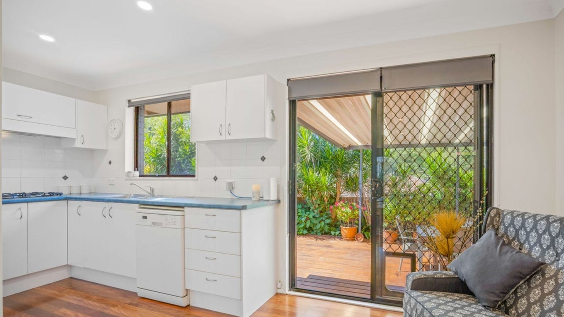 A modern kitchen with white cabinets, a blue countertop, and a sliding glass door leading to a patio with outdoor furniture.