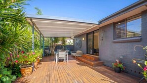 Une terrasse couverte avec un plancher en bois, des sièges d’extérieur et des plantes en pot.