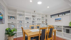 A dining area with a wooden table and chairs, surrounded by white shelving units with various items. - Tranquility At Lighthouse Beach (Port Macquarie)