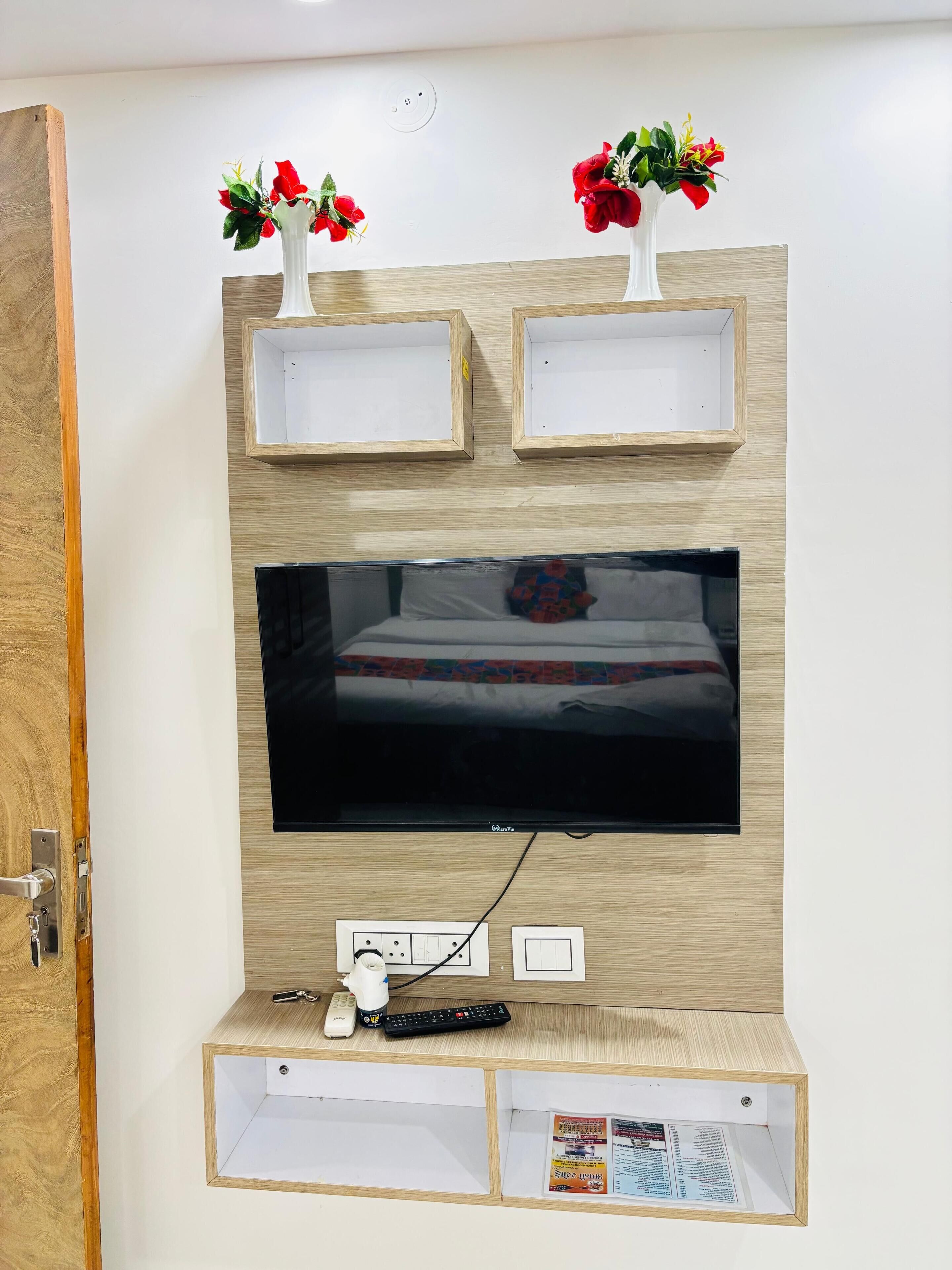 A wall-mounted TV with a wooden frame, two empty shelves above, and a small shelf below with a remote control and a magazine.