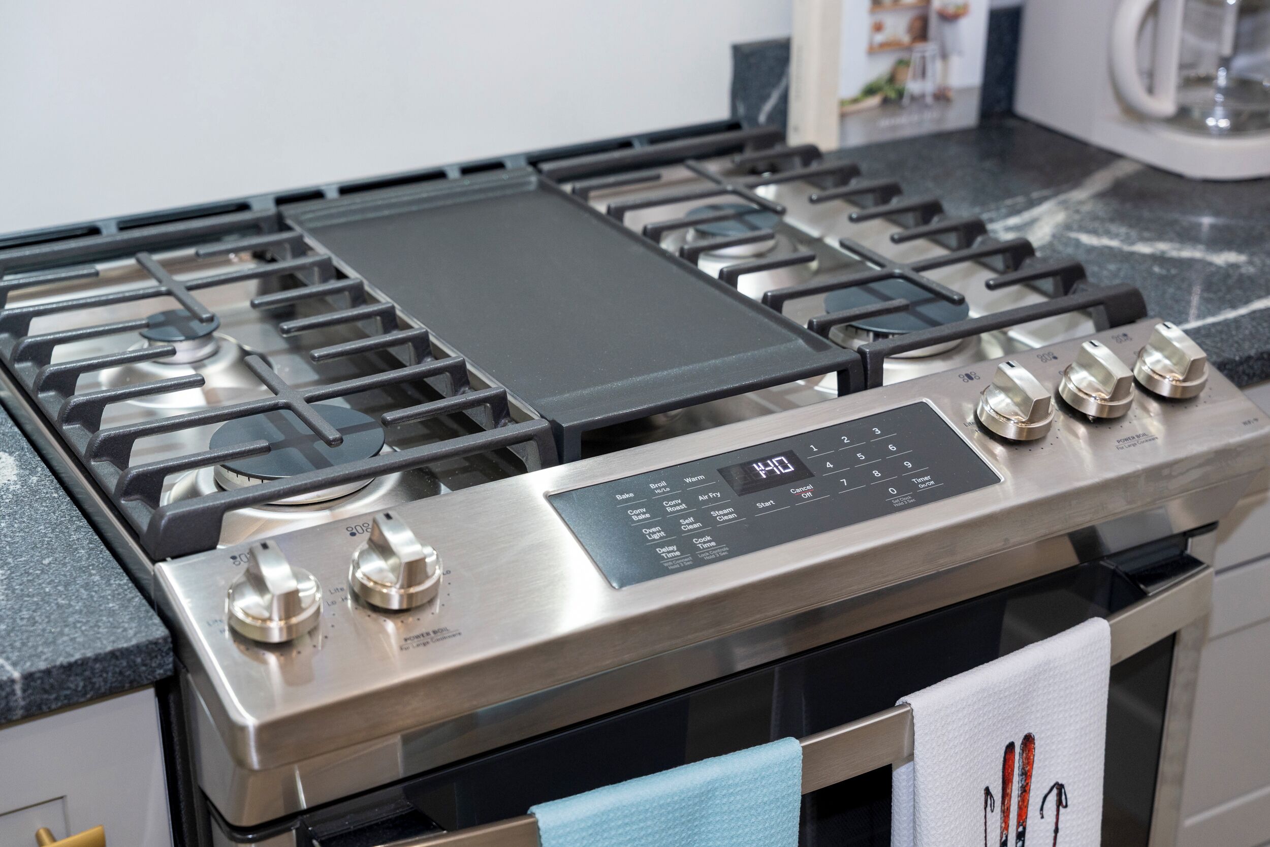 Uma cozinha com fogão de aço inoxidável, painel de controle digital e bancada preta.
