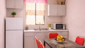 Eine kleine Küche mit Kühlschrank, Mikrowelle und einem Esstisch mit roten Stühlen.