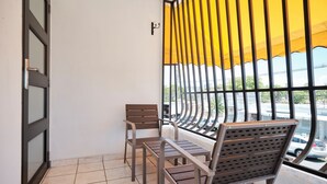 A balcony with two wooden chairs and a small table, a yellow curtain, and a view of the street. - 2-bedroom apartment in serene Hato Rey close to El Coliseum (San Juan)