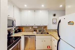 A compact kitchen with white cabinets, a granite countertop, a microwave, a dishwasher, and a refrigerator. - Kitschy Rich Palm Springs - A Ryson Property (Palm Springs)