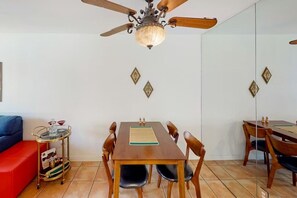 A dining area with a wooden table, chairs, a ceiling fan, and a small side table with a tray. - Kitschy Rich Palm Springs - A Ryson Property (Palm Springs)