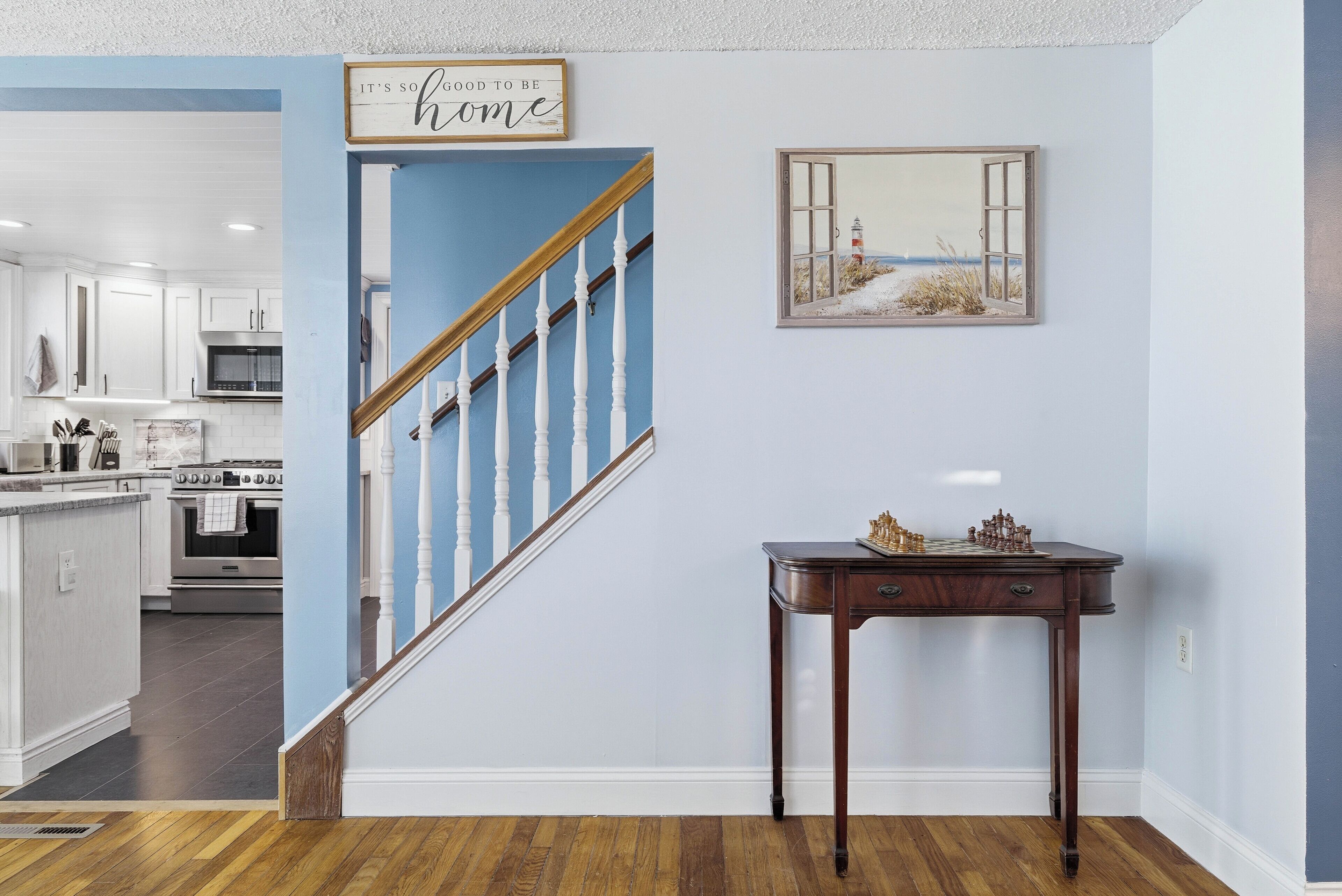 Une cuisine avec des meubles blancs, un escalier en bois et un jeu d’échecs posé sur une table.