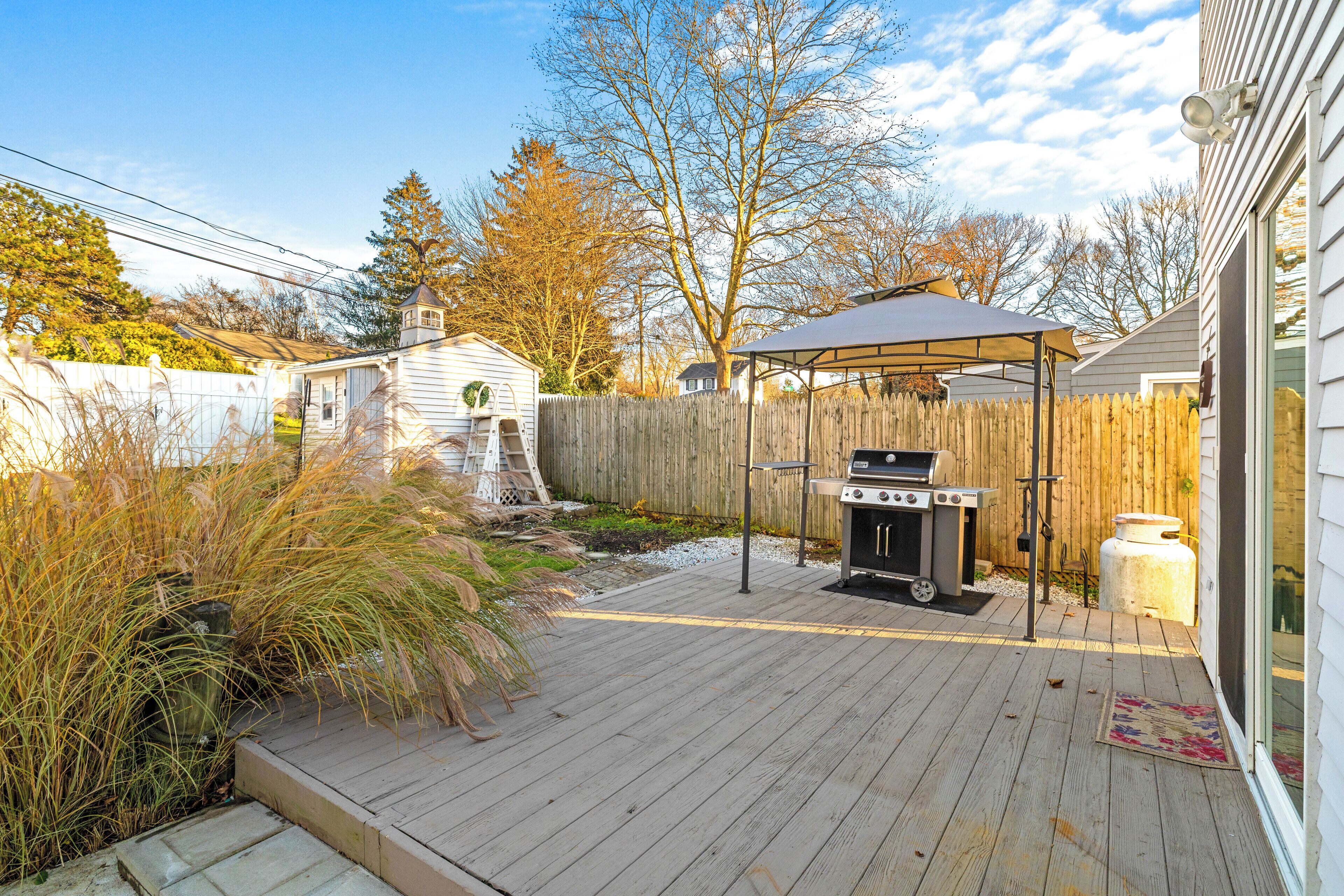 Een achtertuin met een houten terras, een barbecue en een overdekte zithoek.