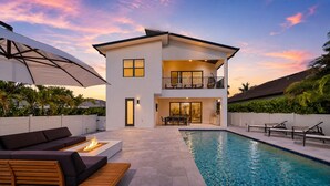 Uma casa de dois andares com piscina, área de estar externa e varanda coberta.