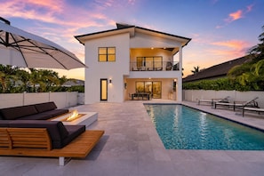 Une maison à deux étages dotée d’une piscine, d’un espace salon extérieur et d’une terrasse couverte.