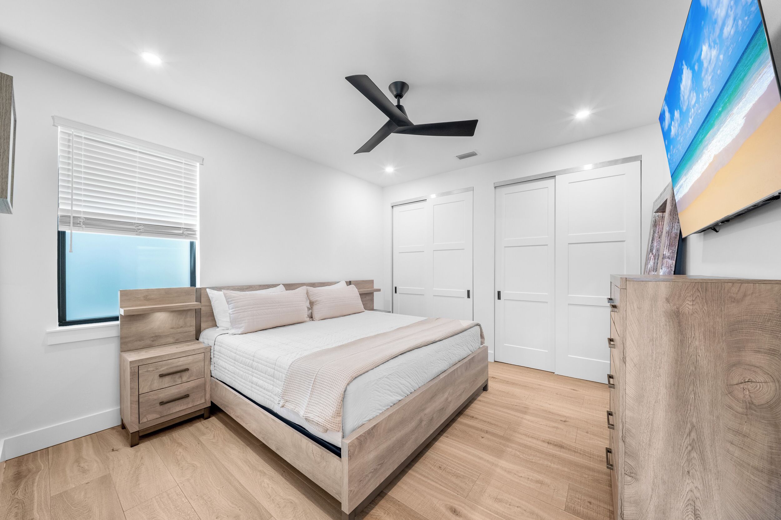 Ein Schlafzimmer mit Bett, Nachttischen, Deckenventilator, Fernseher und Kleiderschrank.