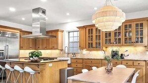 A modern kitchen with wooden cabinets, stainless steel appliances, and a central island with bar stools. - Charming Coastal Getaway – 5 Min to Boardwalk! (Santa Cruz)