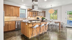 A modern kitchen with wooden cabinets, a stainless steel range hood, and a central island with bar stools. - Charming Coastal Getaway – 5 Min to Boardwalk! (Santa Cruz)
