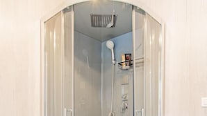 Cabina de bany amb envàs de vidre, plat de dutxa manual i aixeta fixada a la paret.
