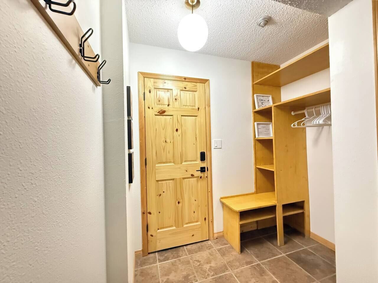 Un pasillo con una puerta de madera, un perchero y un banco de madera.
