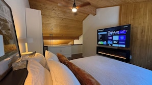 A bedroom with a bed, a TV mounted on the wall, a ceiling fan, and a wooden ceiling. - Summit View Collection |Ski-In ·Hot Tub ·Sleeps 14 (Kimberley)