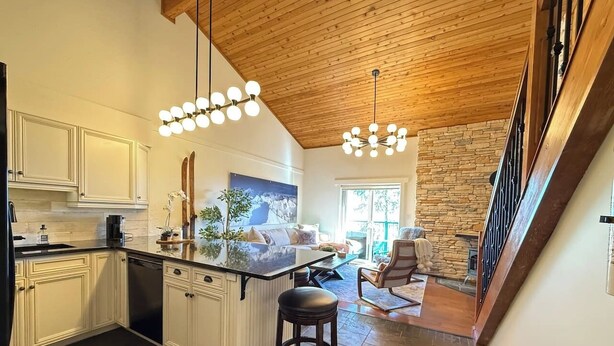 A modern kitchen with white cabinetry, a central island, and a stone fireplace. - Summit View Collection |Ski-In ·Hot Tub ·Sleeps 14 (Kimberley)