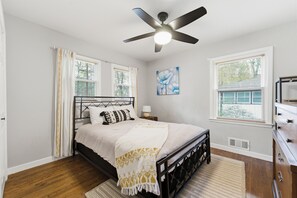 Ein Schlafzimmer mit einem Bett, einem Deckenventilator, einem Fenster mit Jalousien, einem Bild an der Wand und einem Schminktisch.