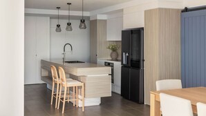 A modern kitchen with a central island, a black refrigerator, and a dining area with wooden chairs. - Luxury Beachfront Burleigh Heads (Burleigh Heads)