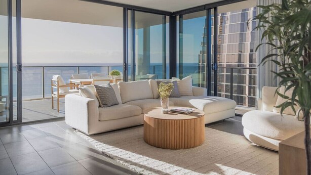 A modern living room with a sofa, coffee table, and chairs, large windows offering a view of the cityscape. - Luxury Beachfront Burleigh Heads (Burleigh Heads)