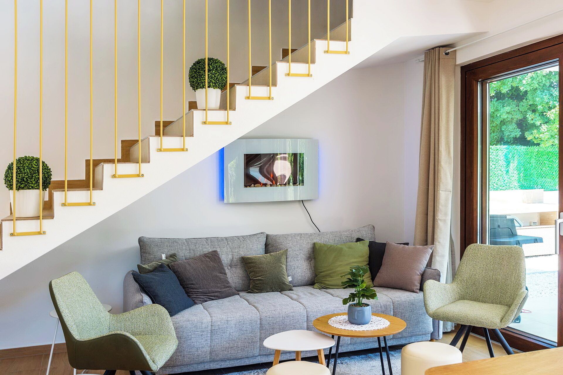 Un salon moderne avec un escalier, un canapé, une table basse et une vue sur la verdure à l’extérieur.