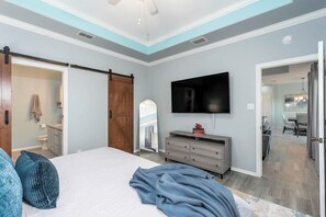 A bedroom with a bed, a dresser, a television, and a sliding door to a bathroom. - Bonita Vista Villa  -27 GH (Laguna Vista)