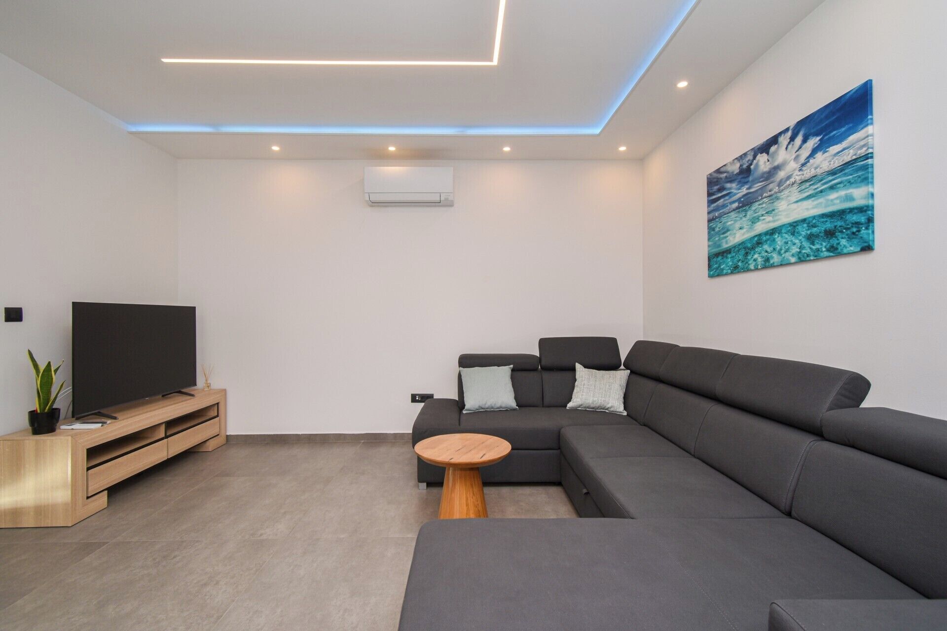 Una sala de estar moderna con un sofá seccional, un televisor de pantalla plana, una mesa de centro de madera y un cuadro en la pared.