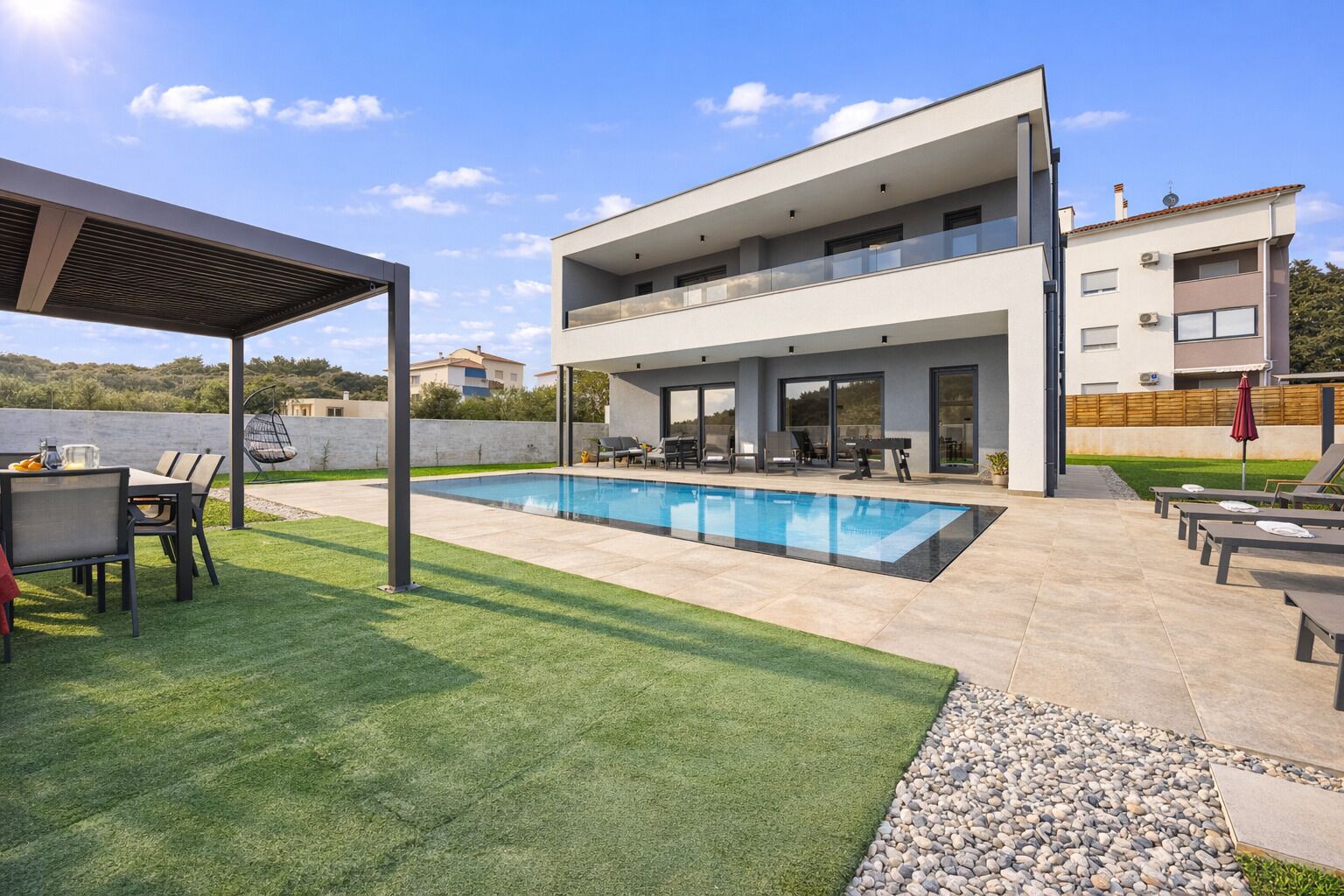 Une maison moderne à deux étages, dotée d’une piscine, d’un espace salon extérieur et d’un patio couvert.