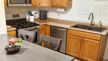 Une cuisine dotée de meubles en bois, d’appareils électroménagers en acier inoxydable, d’un évier et d’une table à manger avec des chaises.