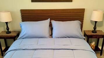 A bed with a wooden headboard, two nightstands with lamps, and a painting of a desert landscape on the wall.