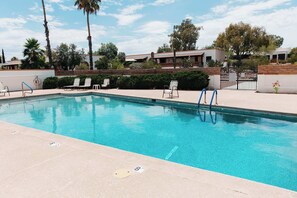 A swimming pool with lounge chairs, a brick wall, and a gate.