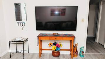 A living room with a TV, a small table, a vase with flowers, and a cat statue.