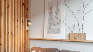 Ein Zimmer mit einer Holzwand, einer gerahmten Architekturzeichnung, einem Holzregal mit Ästen und einer Couch mit gemusterten Kissen.