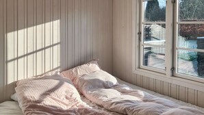 A bedroom with a single bed, a window with a view of the outside, and wooden paneling on the walls.
