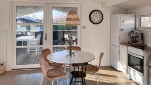 A kitchen with a round table, wicker chairs, a hanging light fixture, a clock, a refrigerator, and an espresso machine.