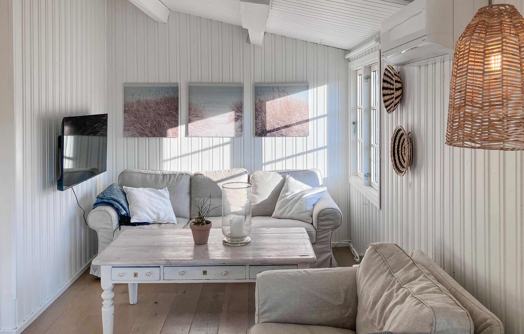 A room with a white striped wall, a grey sofa, a white coffee table with a potted plant, and a woven light fixture.