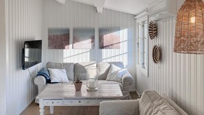 A room with a white striped wall, a grey sofa, a white coffee table with a potted plant, and a woven light fixture.