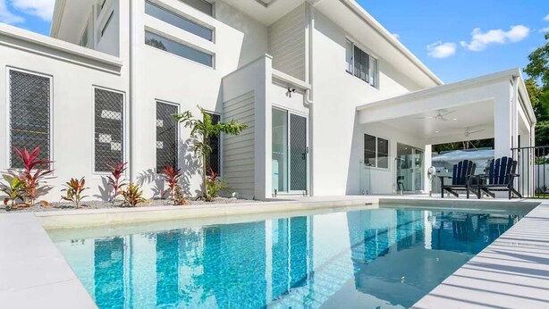 Ein modernes Haus mit Schwimmbad, großen Fenstern und einer überdachten Terrasse.