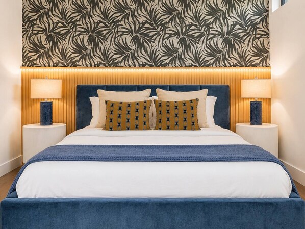 A bed with a blue headboard, white bedding, and patterned pillows.