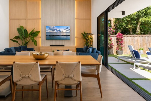 Un espace repas moderne avec une table en bois, des chaises de couleur beige et un téléviseur fixé au mur.