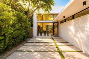 Un bâtiment moderne avec une entrée en verre, un chemin en béton et une haie bien entretenue.