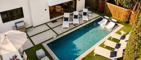 A modern outdoor pool area with lounge chairs and a barbecue grill.
