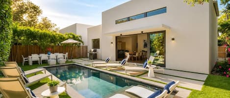 Un espace piscine extérieur moderne, doté de chaises longues et d’un coin repas.