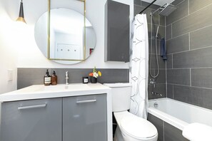 Ett modernt badrum med en vit tvättställ, en toalett, en dusch med en svart duschdraperi och en stor spegel.