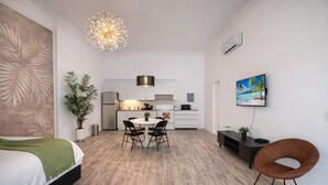 A modern hotel room with a bed, a dining area with a table and chairs, a kitchen area, a large plant, and a painting on the wall. - Miami Beach 1 bedroom Easy Walk to Beach (Miami Beach)