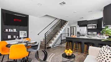 A modern kitchen with a built-in oven, a dining area with orange chairs, and a staircase leading to an upper level.