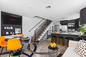 Een moderne keuken met een inbouwoven, een eethoek met oranje stoelen en een trap naar een hoger niveau.