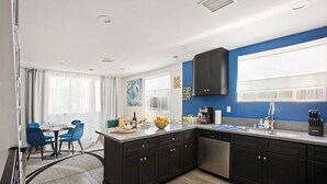 Eine moderne Küche mit dunklen Schränken, einem großen Fenster und einem Essbereich mit blauen Stühlen.