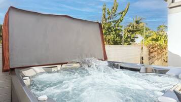 A hot tub with a cover, surrounded by outdoor seating and a white wall.