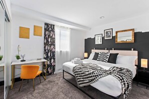A hotel room with a bed, a desk, a chair, a window with curtains, and a wall with framed pictures. - LA Oasis|Jacuzzi|Parking|Fireplace| Prime Location (Los Angeles)